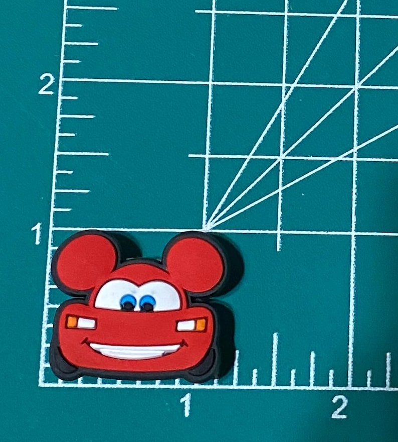 May include: Red cartoon car with Mickey Mouse ears, smiling with blue eyes. The car has headlights and a grill.