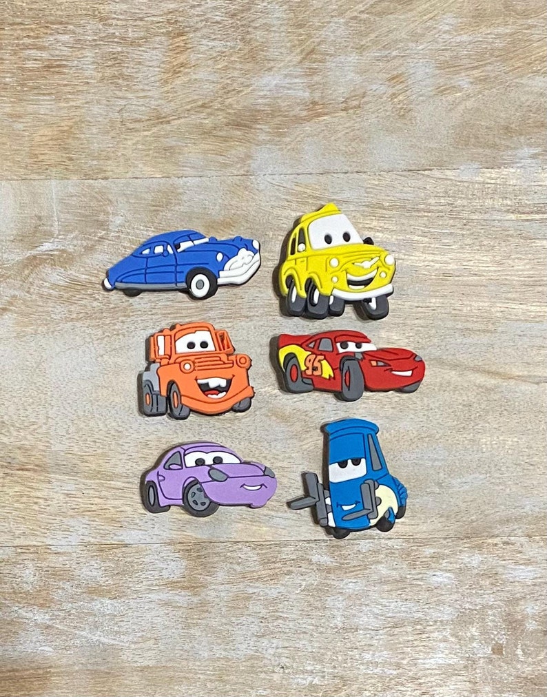 May include: Six colourful cartoon car character figurines. The characters include Mater, Lightning McQueen, Tow Mater, a purple sports car, a yellow taxi, and a blue car.