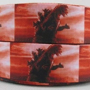 May include: Two rolls of ribbon featuring a Godzilla design against a red and orange sunset background. The ribbon is a repeating pattern of the iconic monster, perfect for crafting or adding a unique touch to gifts.