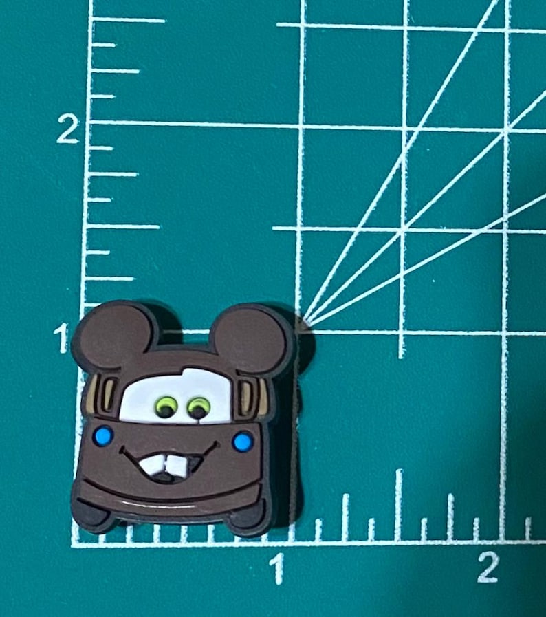 May include: Brown cartoon car with Mickey Mouse ears, green eyes, and blue accents. The car is smiling with a toothy grin.