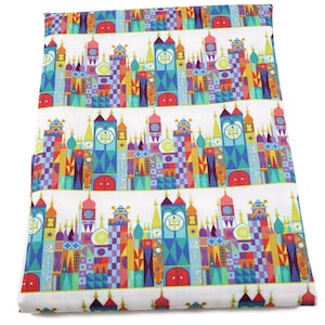 Puede incluir: Tela blanca con un patrón repetido de edificios de castillo estilizados y coloridos. Los edificios del castillo están hechos de varias formas geométricas y colores, incluyendo rojo, azul, verde, amarillo y morado.