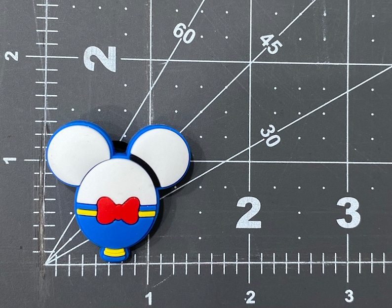 May include: Blue and white rubber charm with a red bow, shaped like a cartoon character with Mickey Mouse ears.