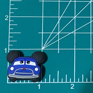 May include: Blue car with black Mickey Mouse ears, a red nose, and white headlights. The car is on a green cutting mat with white lines.