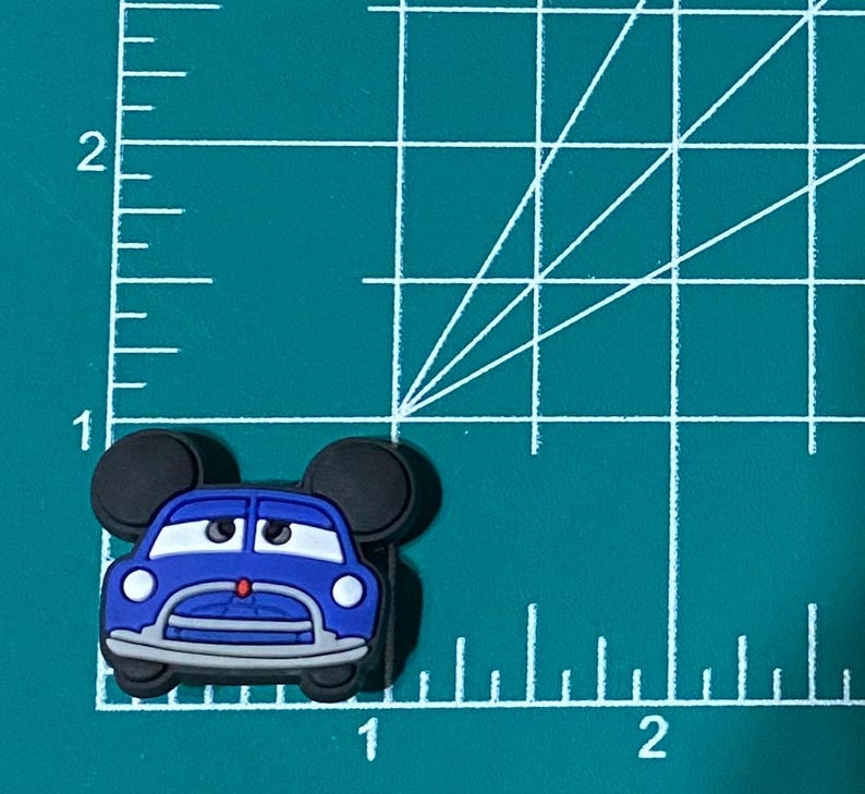 May include: Blue car with black Mickey Mouse ears, a red nose, and white headlights. The car is on a green cutting mat with white lines.