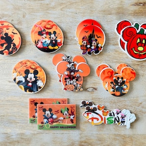 May include: A set of 10 Halloween-themed round and oval-shaped coasters featuring Mickey Mouse and other Disney characters. The coasters are decorated with orange, black, and white colors and feature images of Mickey Mouse, Minnie Mouse, Goofy, and Donald Duck. The coasters are perfect for adding a touch of Disney magic to your home decor.