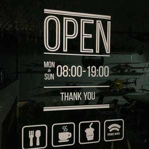Puede incluir: Un letrero blanco sobre un fondo oscuro muestra la palabra "OPEN" en letras en negrita. Debajo, indica el horario de apertura de 8:00 a 19:00, de lunes a domingo. También hay iconos de tenedor y cuchara, café, una bebida de café y Wi-Fi gratis.