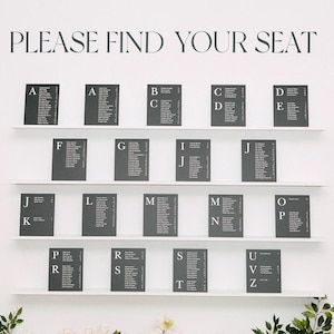 Op de afbeelding: Een witte plattegrond met de tekst "PLEASE FIND YOUR SEAT" boven rijen met gastennamen. De plattegrond is versierd met witte bloemen en groen aan de basis.