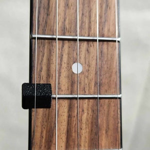 May include: Close-up of a wooden guitar fretboard with a white dot inlay and a black capo attached to the first fret.