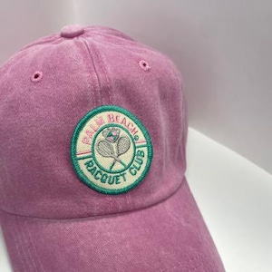 May include: A pink baseball cap with a green, white and pink embroidered patch that says "Calm Beach Racquet Club".