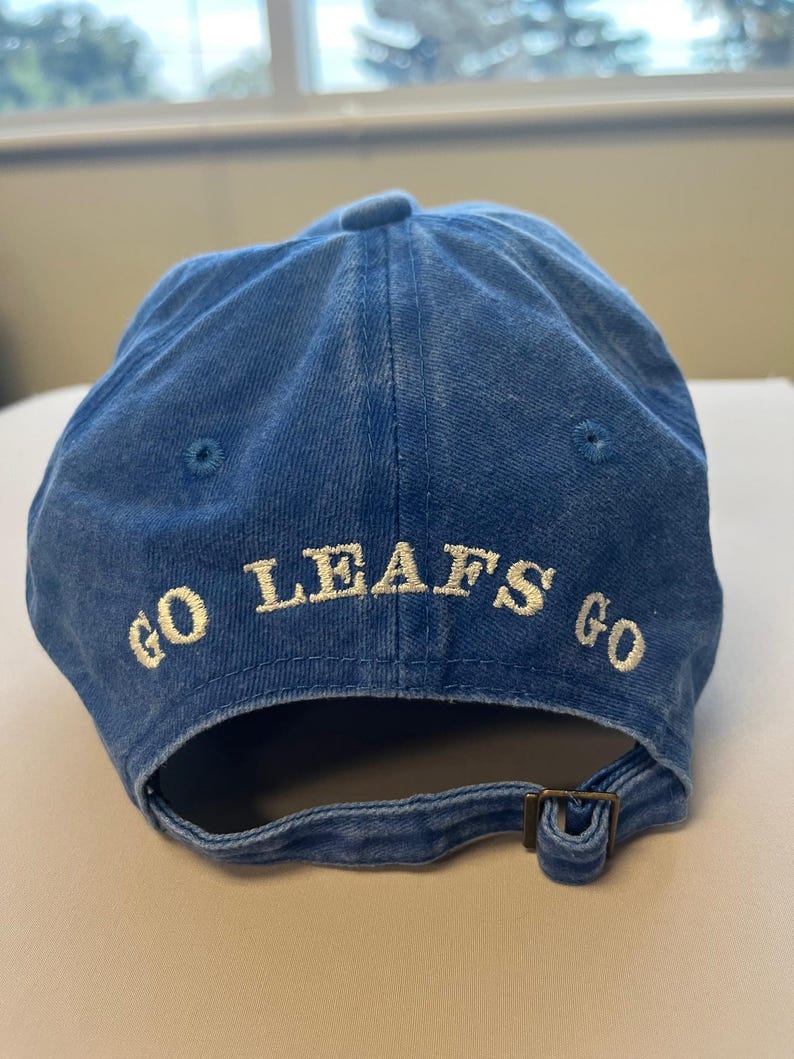 Pu&ograve; includere: Cappellino da baseball blu con le parole "GO LEAFS GO" ricamate in bianco. Il cappellino ha una visiera curva e una chiusura con fibbia metallica regolabile. Realizzato in tessuto morbido e usurato.
