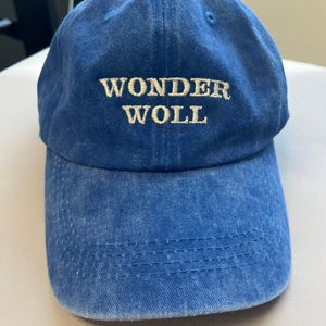 Pu&ograve; includere: Un cappellino da baseball blu con la scritta ricamata "WONDER WOLL" in un colore pi&ugrave; chiaro. Il cappellino ha una visiera curva e una chiusura con cinturino in tessuto. Il cappello &egrave; realizzato in un materiale morbido e strutturato.