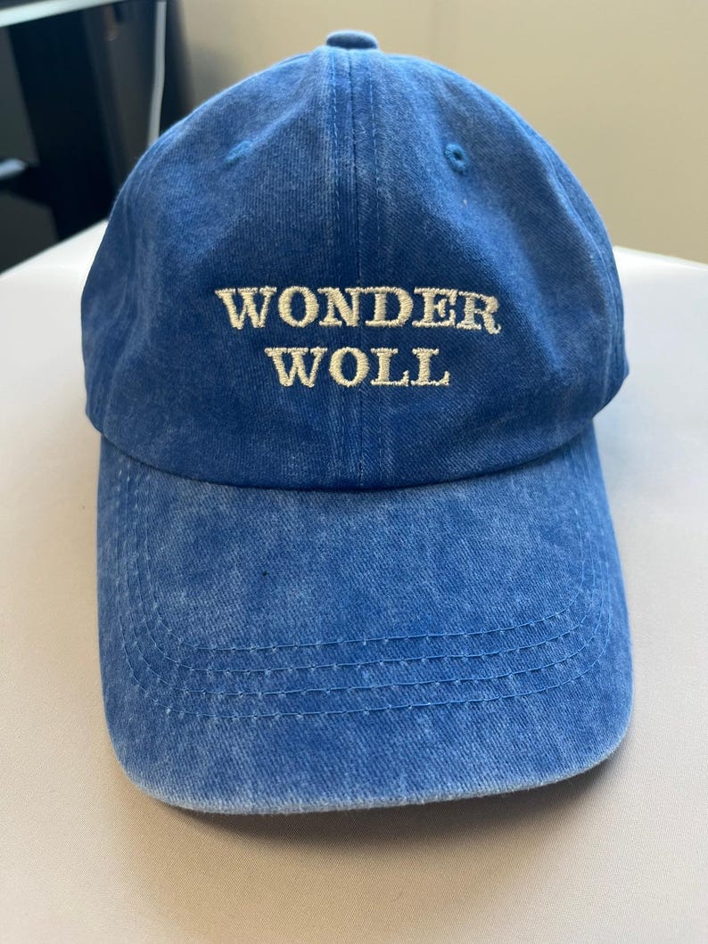 Pu&ograve; includere: Un cappellino da baseball blu con la scritta ricamata "WONDER WOLL" in un colore pi&ugrave; chiaro. Il cappellino ha una visiera curva e una chiusura con cinturino in tessuto. Il cappello &egrave; realizzato in un materiale morbido e strutturato.