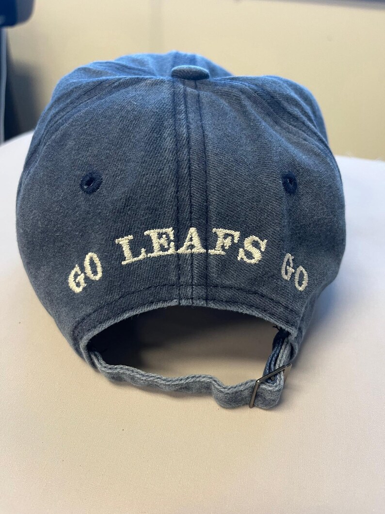 May include: A denim blue baseball cap with the words "GO LEAFS GO" embroidered in white across the back. The cap has a curved brim and an adjustable strap.