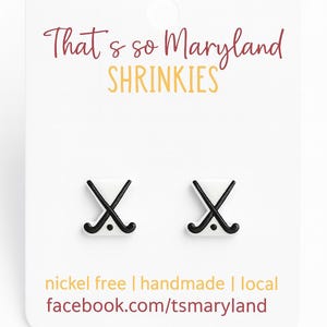 May include: White Shrinkies earrings with black hockey stick design. The card reads "That's so Maryland Shrinkies" in maroon and yellow. The card also states "nickel free | handmade | local facebook.com/tsmaryland".