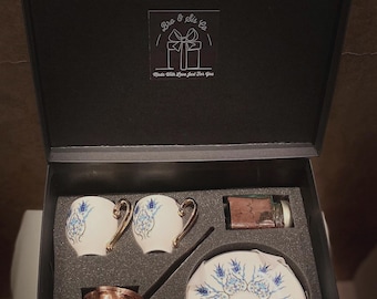 May include: A black gift box with a copper Turkish coffee pot, two white and blue patterned coffee cups, a saucer with a matching pattern, and a small jar of coffee grounds. The box has a label that reads "Bro & Sis Co. Made With Love Just For You."