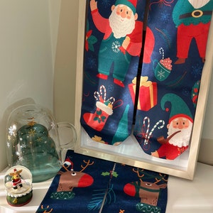 Pode incluir: Dois pares de meias de Natal azuis com um padrão festivo que apresenta o Papai Noel, uma rena e um gnomo. As meias são exibidas em uma superfície branca.