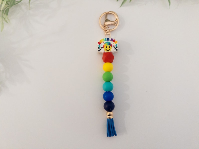 May include: Rainbow beaded keychain with a gold charm featuring a smiley face and the words "Think Happy".