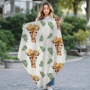 May include: A white throw blanket with a repeating pattern of giraffe faces wearing flower crowns and green palm leaves.