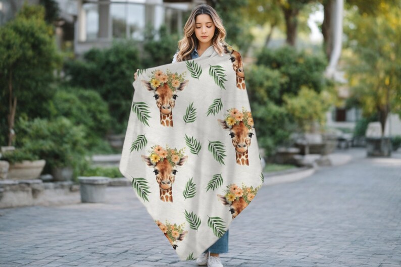 May include: A white throw blanket with a repeating pattern of giraffe faces wearing flower crowns and green palm leaves.