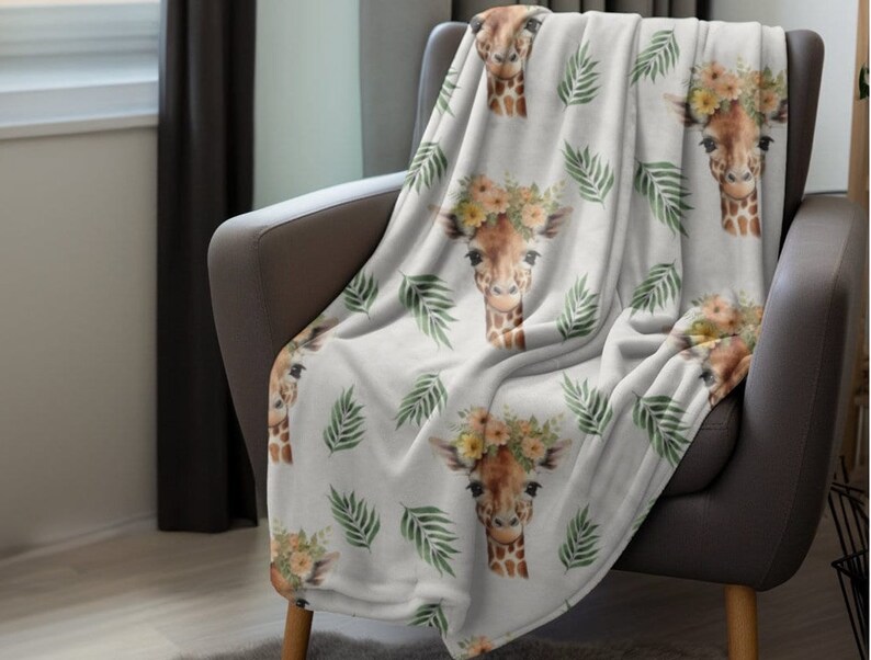 May include: A white throw blanket with a repeating pattern of giraffes wearing flower crowns and green palm leaves.