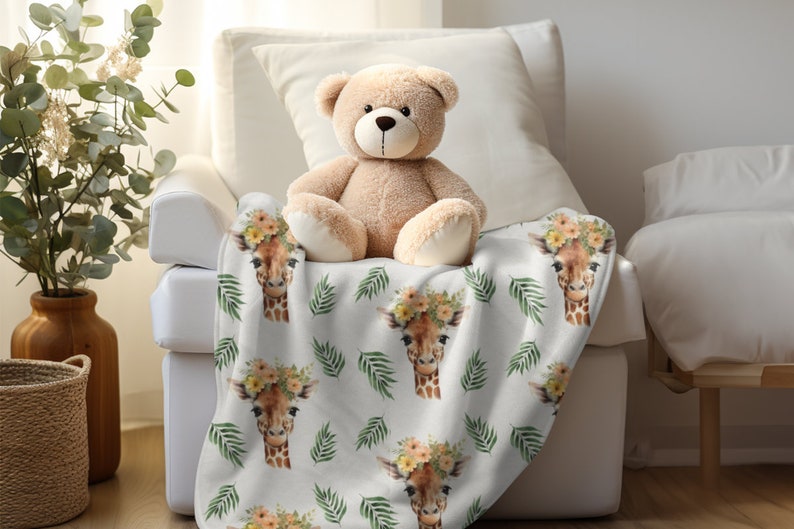 May include: White plush throw blanket with a repeating pattern of giraffe faces wearing floral crowns and green palm leaves. A brown teddy bear is sitting on the blanket.