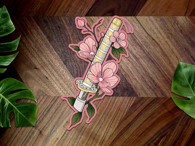 May include: A pink and yellow sticker with a stylized illustration of a katana sword wrapped in a floral design. The sword is surrounded by pink flowers and green leaves.