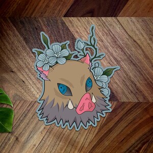 May include: A blue and brown cartoon boar head with a crown of blue flowers. The boar has a pink snout and sharp teeth. The boar's eyes are blue and have a white highlight.