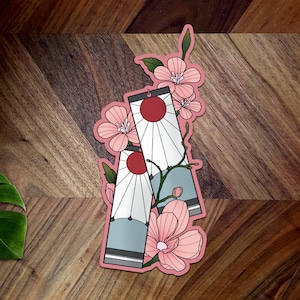 May include: Two pink and white patterned stickers with a red sun and white rays. The stickers are surrounded by pink cherry blossoms.
