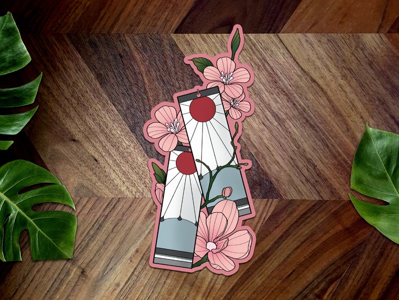 May include: Two pink and white patterned stickers with a red sun and white rays. The stickers are surrounded by pink cherry blossoms.