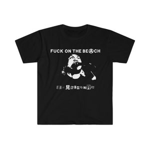 May include: Black t-shirt featuring a white graphic. The graphic includes the text "FUCK ON THE BEACH" above a white image of a person singing into a microphone. Below the image are Japanese characters.