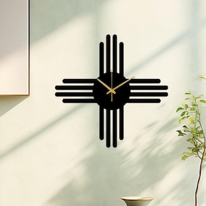 May include: Black wall clock with a gold clock face and hands, shaped like the Zia symbol, a traditional symbol of the Pueblo people of New Mexico.