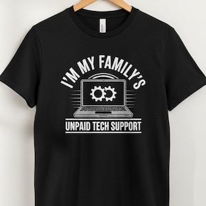 May include: Black t-shirt with the text "I'M MY FAMILY'S UNPAID TECH SUPPORT" in white. The design features a laptop with gear icons on the screen. The shirt is hanging on a wooden hanger.