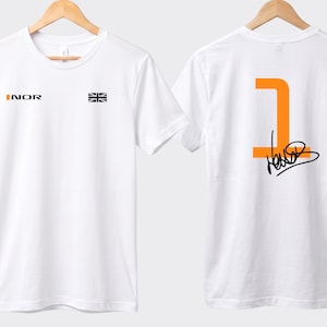 May include: White t-shirt with the word "INOR" in orange and a Union Jack flag on the front. The back of the shirt displays a large orange number "1" and a black signature.