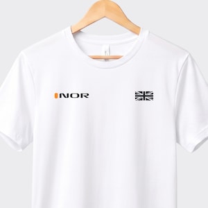 May include: White t-shirt featuring the word "INOR" in orange and black text on the left chest. A small black and white Union Jack flag is on the right chest. The shirt is displayed on a wooden hanger.