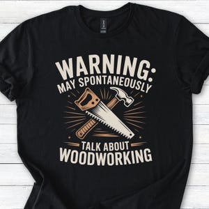 Op de afbeelding: Zwart T-shirt met een grafisch ontwerp over houtbewerking. Het ontwerp toont een zaag en een hamer met de tekst "WARNING: MAY SPONTANEOUSLY TALK ABOUT WOODWORKING" in het wit. Het T-shirt is gemaakt van zacht materiaal.