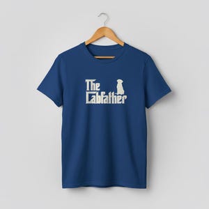 Op de afbeelding: Marineblauw T-shirt met de tekst "The Labfather" in verweerd gebroken wit en een silhouet van een hond. Het T-shirt hangt aan een houten kleerhanger.