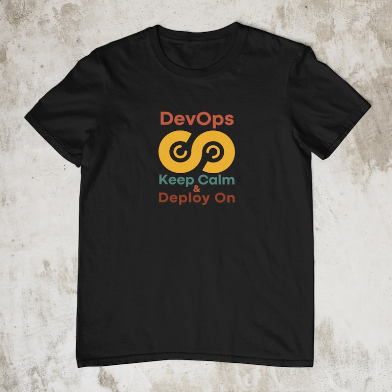K&ouml;nnte beinhalten: Schwarzes T-Shirt mit einem gelben Unendlichkeitszeichen und dem Text "DevOps Keep Calm & Deploy On" in Rot, Orange und T&uuml;rkis.