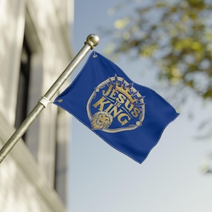 Könnte beinhalten: Eine blaue Flagge mit dem goldenen Schriftzug "JESUS IS KING", einem Löwen und einem Kronen-Design. Die Flagge ist an einer silbernen Stange befestigt und weht im Wind. Es ist ein religiöser Artikel.