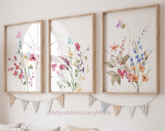 May include: Three framed watercolor paintings of colorful flower bouquets with butterflies. The paintings are hung on a white wall with a string of fabric flags hanging below them.