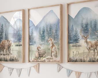 Op de afbeelding: Drie ingelijste wandkunstwerken met aquarelillustraties van bosdieren. De linker print toont een bruine beer, het midden een vos en eekhoorn, en de rechter een hert. Elke print toont blauwe bergen en dennenbomen in een bosrijke omgeving.