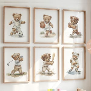 May include: A set of six framed wall art prints featuring watercolor-style teddy bears engaged in various sports, including soccer, basketball, football, golf, baseball, and hockey, each displayed in a light wood frame against a white wall.