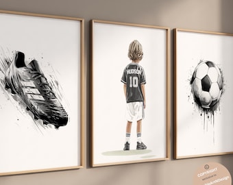 Puede incluir: Tres láminas decorativas enmarcadas con temática de fútbol. La lámina de la izquierda muestra una bota de fútbol en blanco y negro con efectos de salpicaduras de tinta. La central muestra a un niño con una camiseta con el nombre HUDSON y el número 10. La de la derecha muestra un balón de fútbol.
