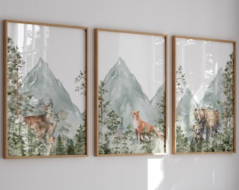 Op de afbeelding: Een set van drie verticale wandposters in lichte houten lijsten. Elke print bevat een aquarelillustratie van een boslandschap met groene bergen, dennenbomen en wilde dieren, waaronder herten, een vos, een konijn en een bruine beer.
