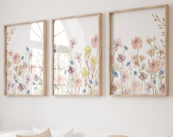 May include: Three framed watercolor prints of a field of wildflowers in shades of pink, blue, and yellow. The prints are arranged in a row on a white wall.
