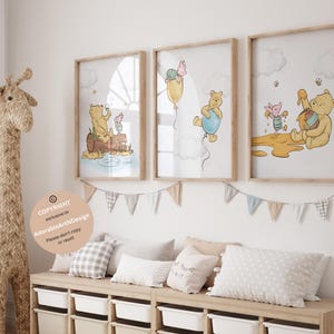 Pu&ograve; includere: Tre stampe incorniciate di Winnie the Pooh con illustrazioni di Winnie the Pooh e Piglet. Le stampe sono appese a una parete bianca sopra una panca di legno con cuscini. Una statuetta di giraffa intrecciata &egrave; in piedi sul pavimento a sinistra della panca.