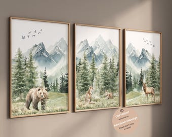 Op de afbeelding: Een set van drie ingelijste wandkunstprints met aquarellandschappen van bergen, dennenbossen en wilde dieren. De eerste print toont een beer, de tweede een vos en de derde een hert. Elke print is voorzien van een lijst van lichtgekleurd hout.