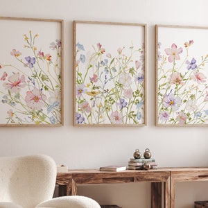 K&ouml;nnte beinhalten: Drei gerahmte Aquarellbilder von rosa, lila und blauen Wildblumen auf wei&szlig;em Hintergrund. Die Bilder sind in einer Reihe an einer wei&szlig;en Wand angeordnet.