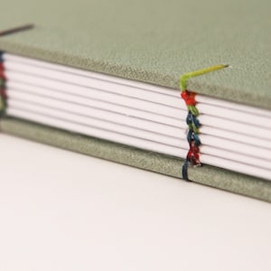 May include: A green fabric-covered journal with colorful thread stitching along the spine.