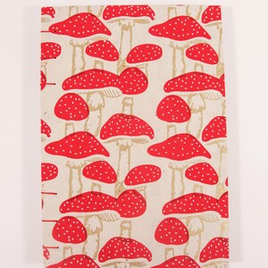 May include: A notebook with a red and white mushroom pattern on the cover. The mushrooms are printed on a cream-colored background.