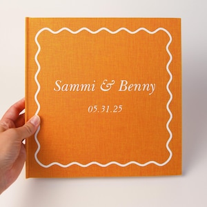 Puede incluir: Un libro naranja con texto blanco y un borde ondulado blanco. El texto dice "Sammi & Benny" encima de la fecha "05.31.25". El libro está sostenido por una mano.